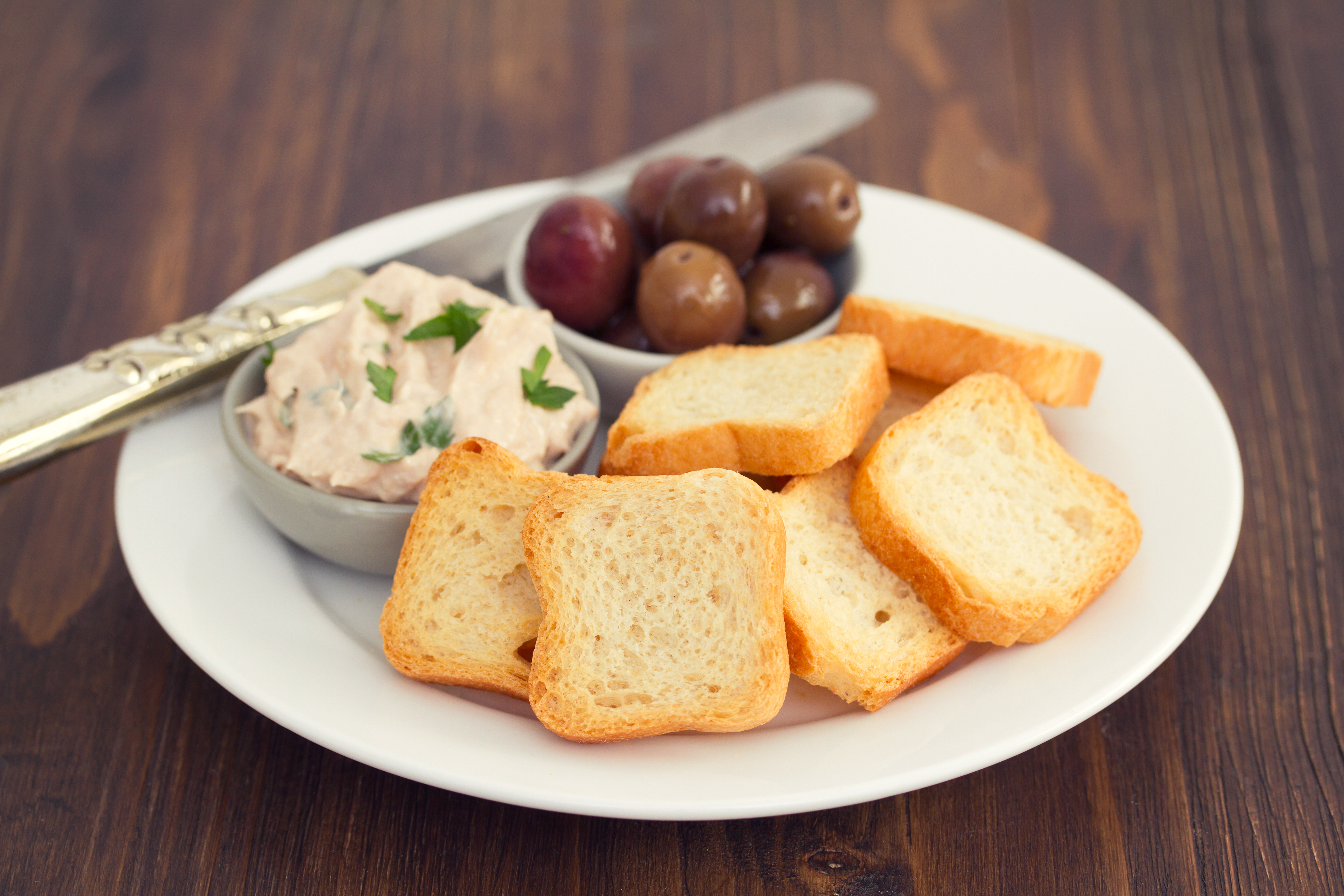 toasts with fish pate and olives on white plate
